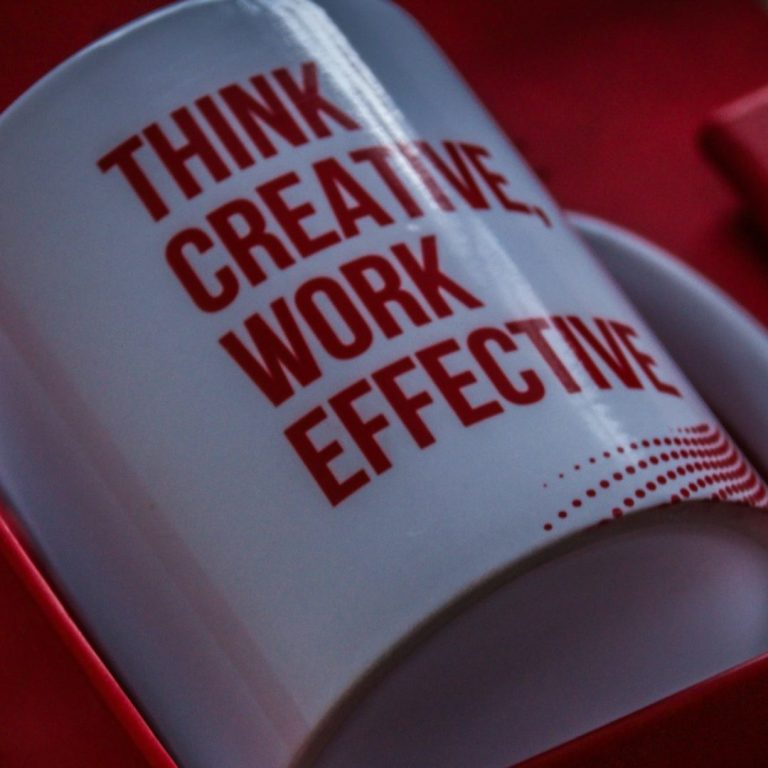 Taza blanca con el texto "Think creative, work effective" en rojo.